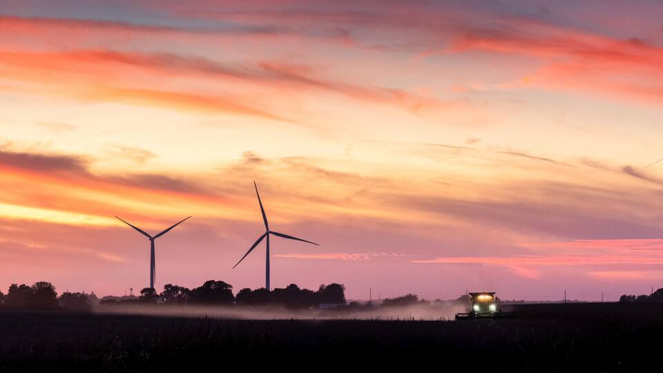 A sunset over a field with wind turbines and a combine harvester.