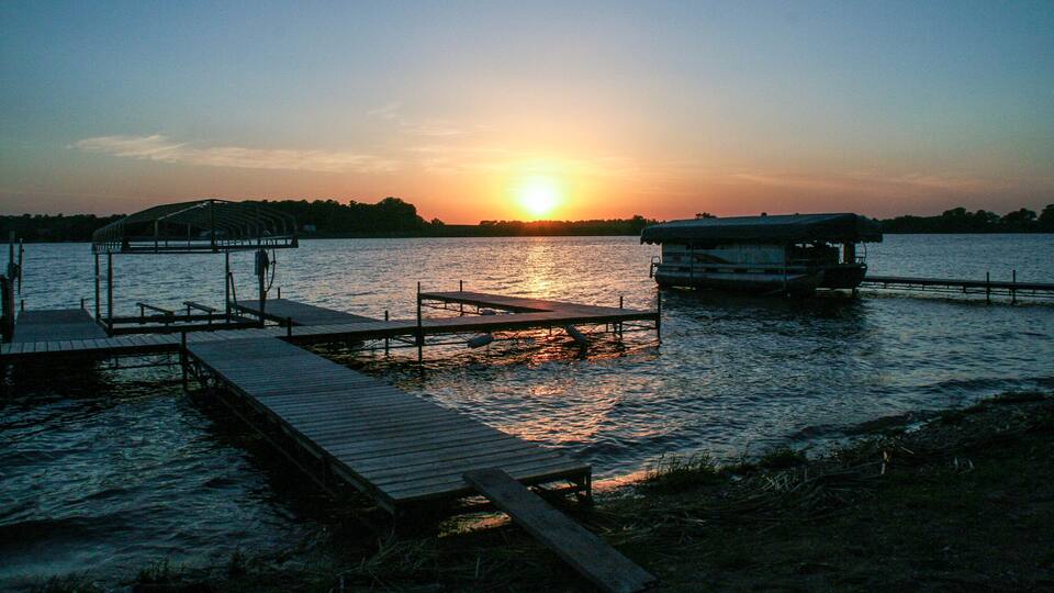 A sunset over a calm lake with wooden docks and a boat.