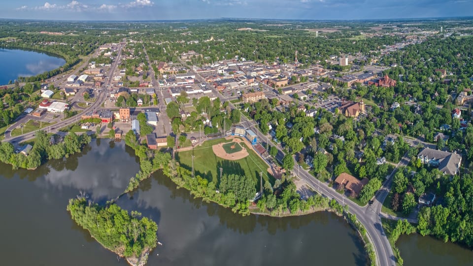 An aerial view of a town with a baseball field, a lake, and surrounding greenery.