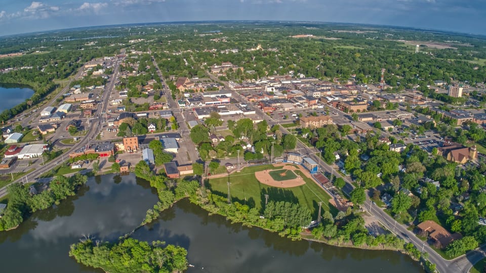 An aerial view of a town with a baseball field, a lake, and surrounding greenery.