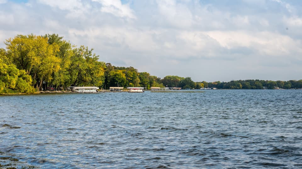 A calm lake with boats, trees, and a cloudy sky.