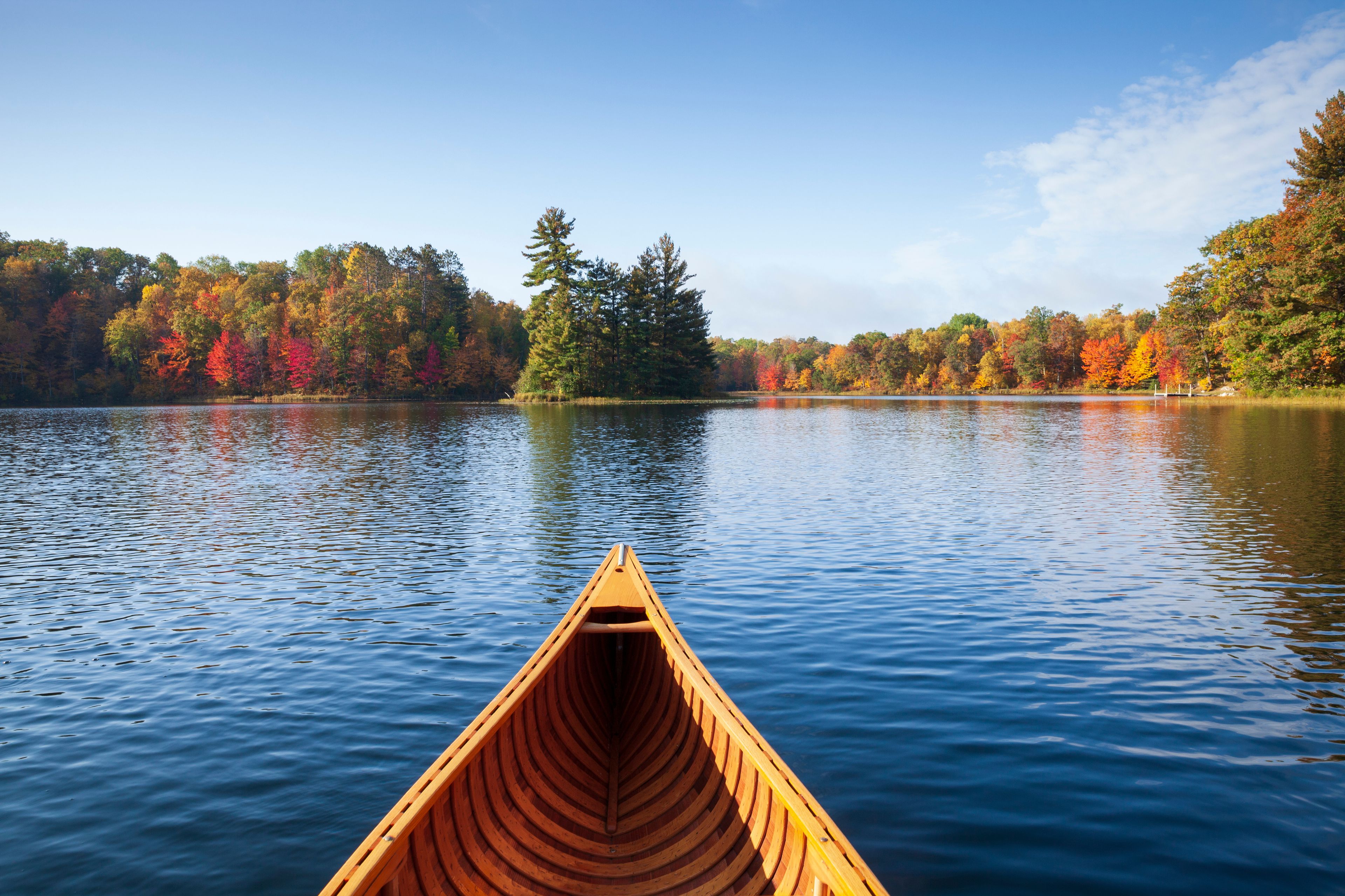 Wooden canoe moves on a blue lake with trees in autumn color and a small island in northern Minnesota