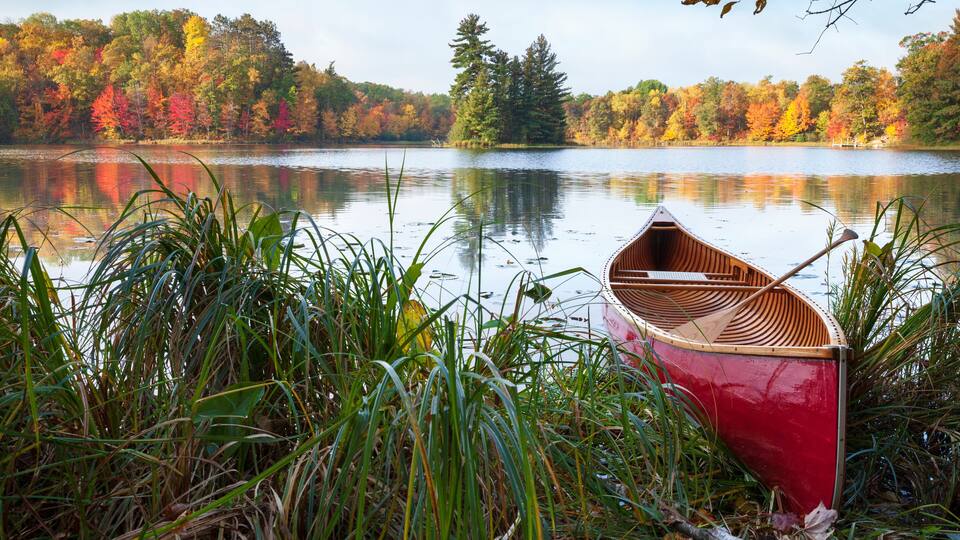 A red canoe on a calm lake surrounded by autumn foliage.