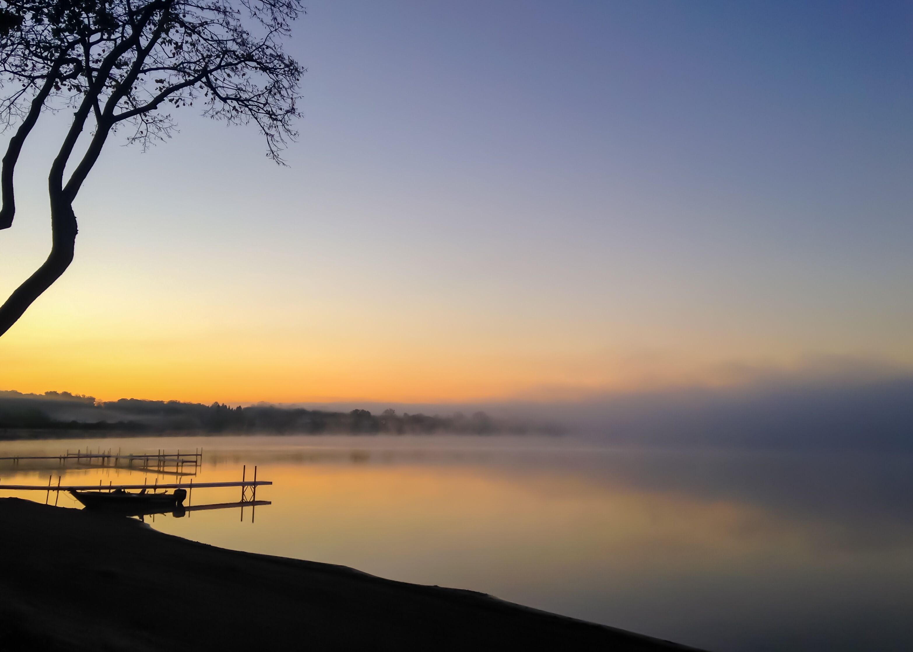 Foggy sunrise over Detroit Lake in Minnesota in the USA framed by a tree and dock