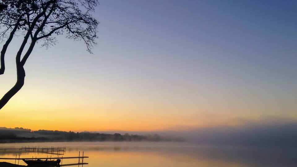 Foggy sunrise over Detroit Lake in Minnesota in the USA framed by a tree and dock