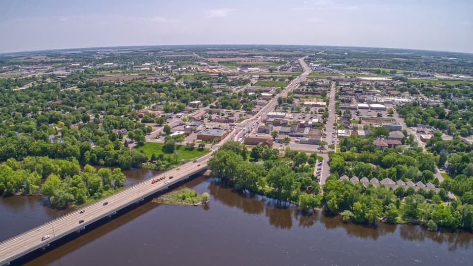 An aerial view of a town with a river, a bridge, and surrounding greenery.