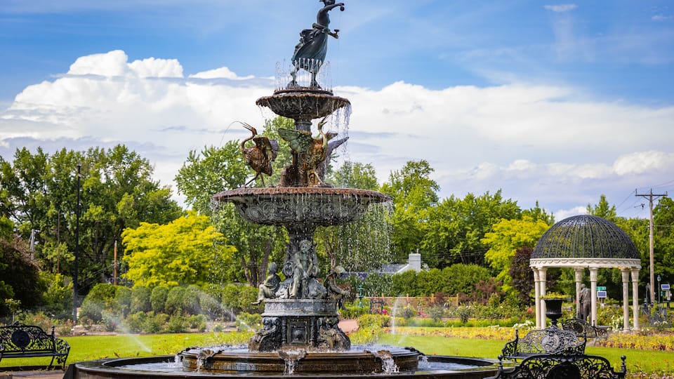A multi-tiered fountain with statues, surrounded by lush greenery and a gazebo.
