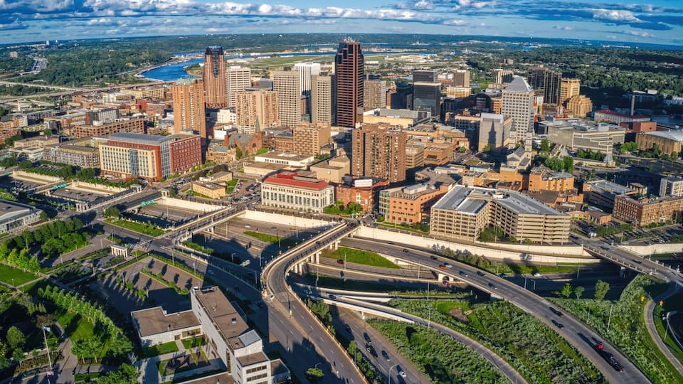 An aerial view of a city with a river, high-rise buildings, and a highway interchange.