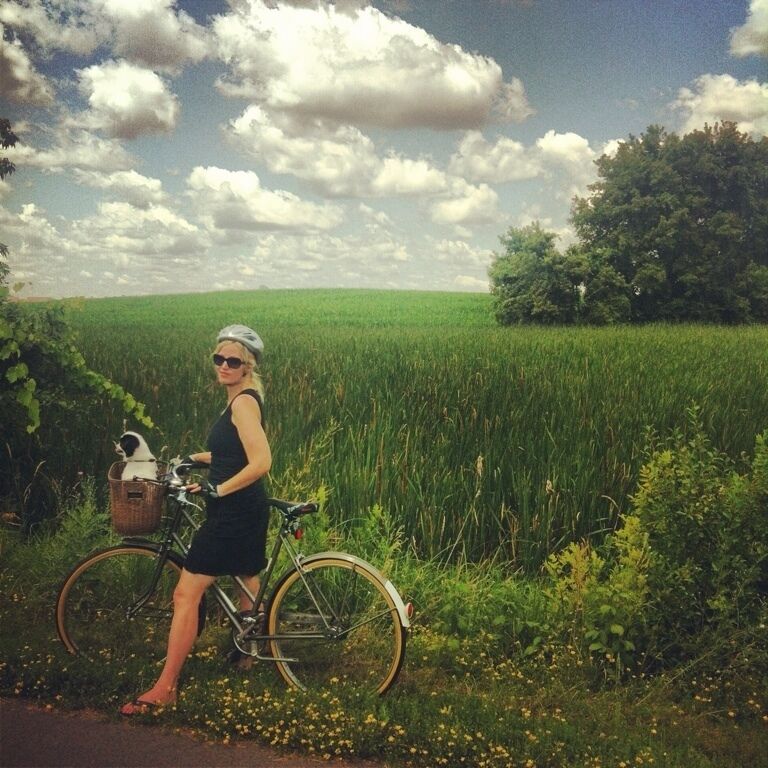 A woman standing next to a bicycle in a field with a basket containing a cat.
