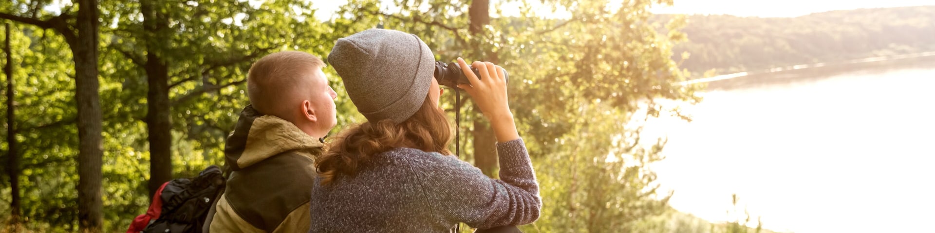 A young man and his girlfriend are sitting looking at the river through binoculars.