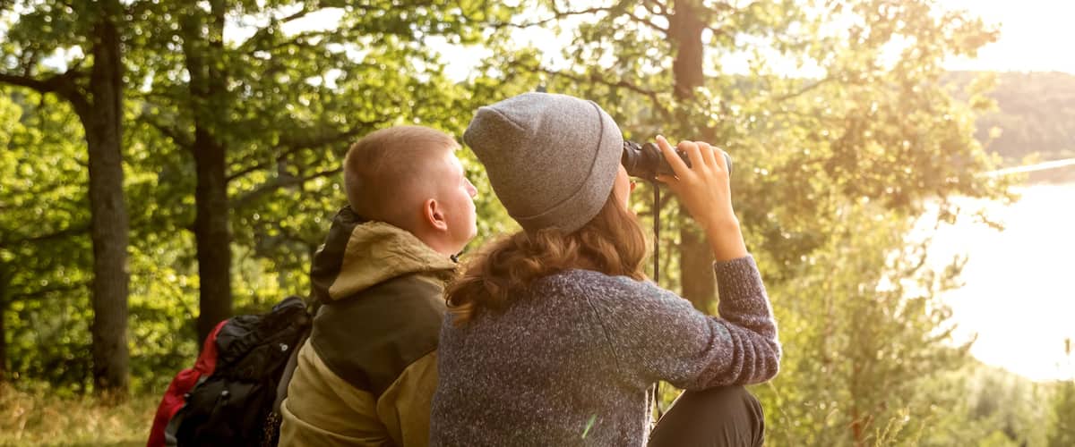 A young man and his girlfriend are sitting looking at the river through binoculars.