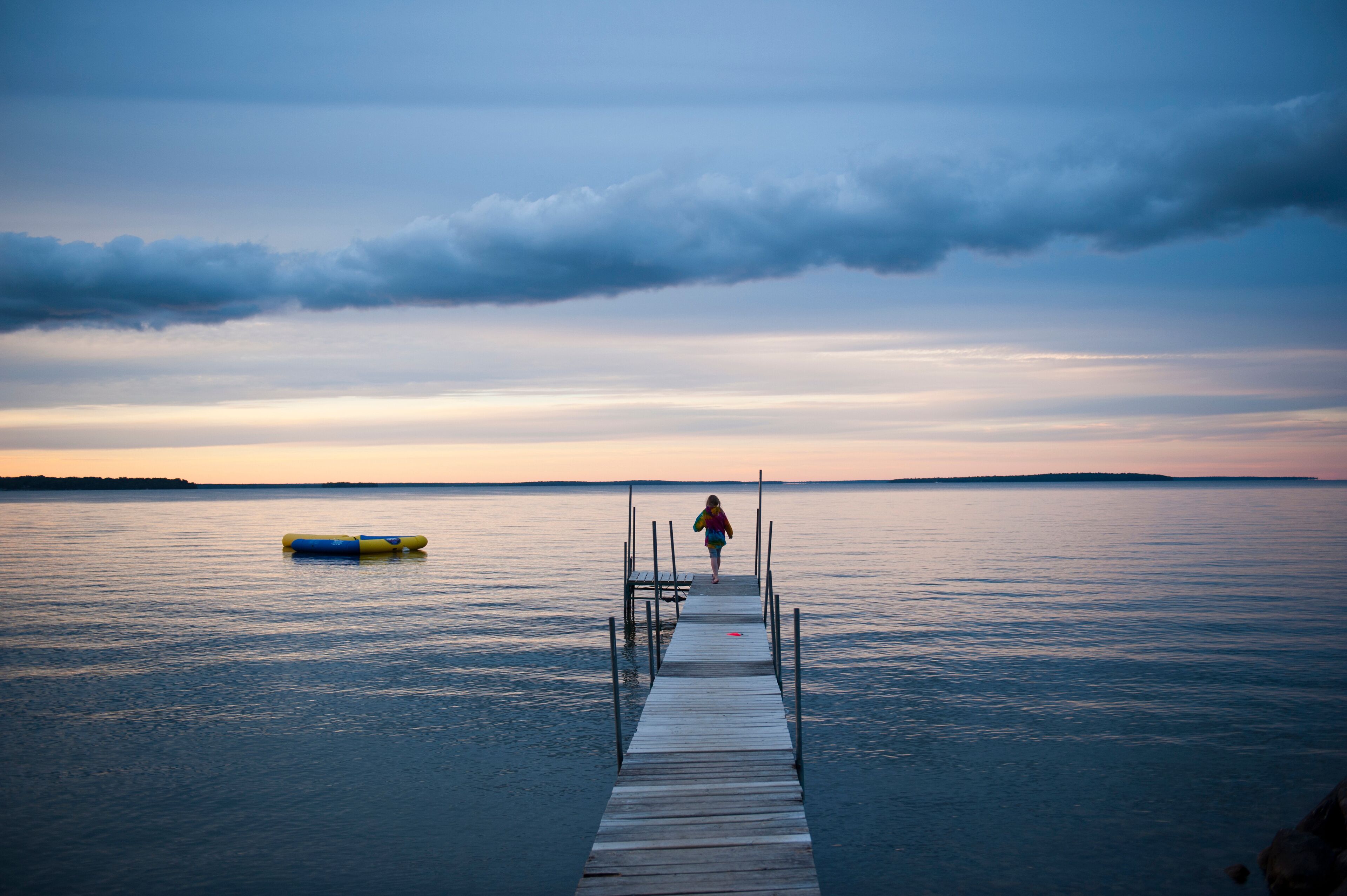 Lone person walking to the end of a dock on a tranquil lake at dusk, Leech Lake near Walker, Minnesota, USA; Walker, Minnesota, United States of America