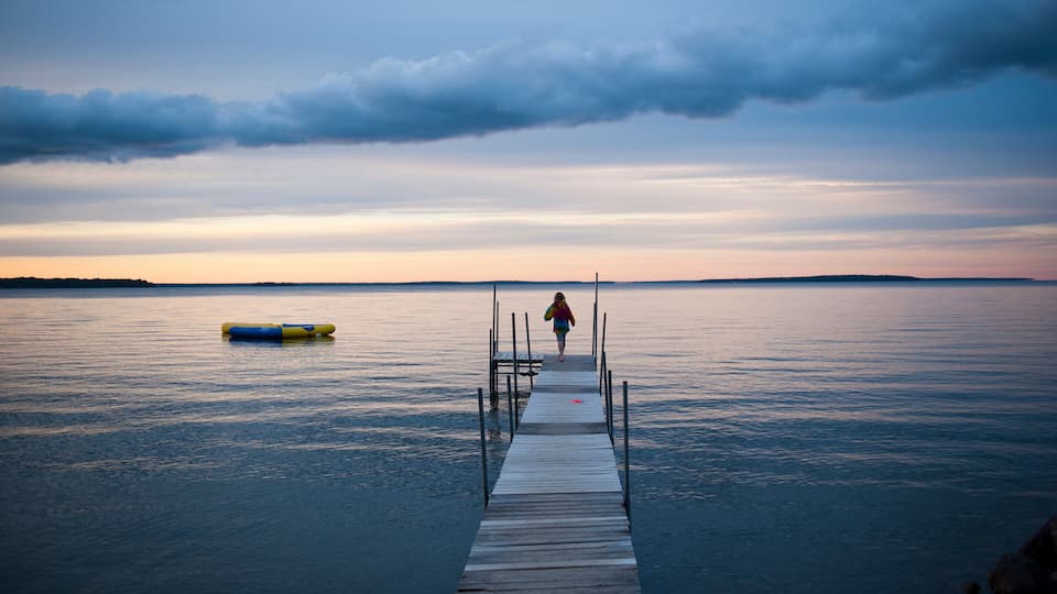 A wooden pier extending into calm water with a person walking towards the horizon.