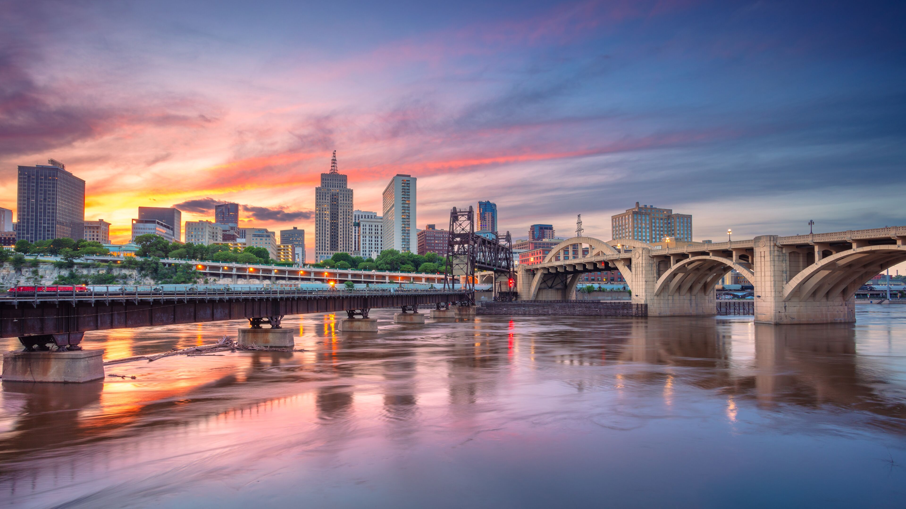 A city skyline at sunset with a bridge reflecting in the water.