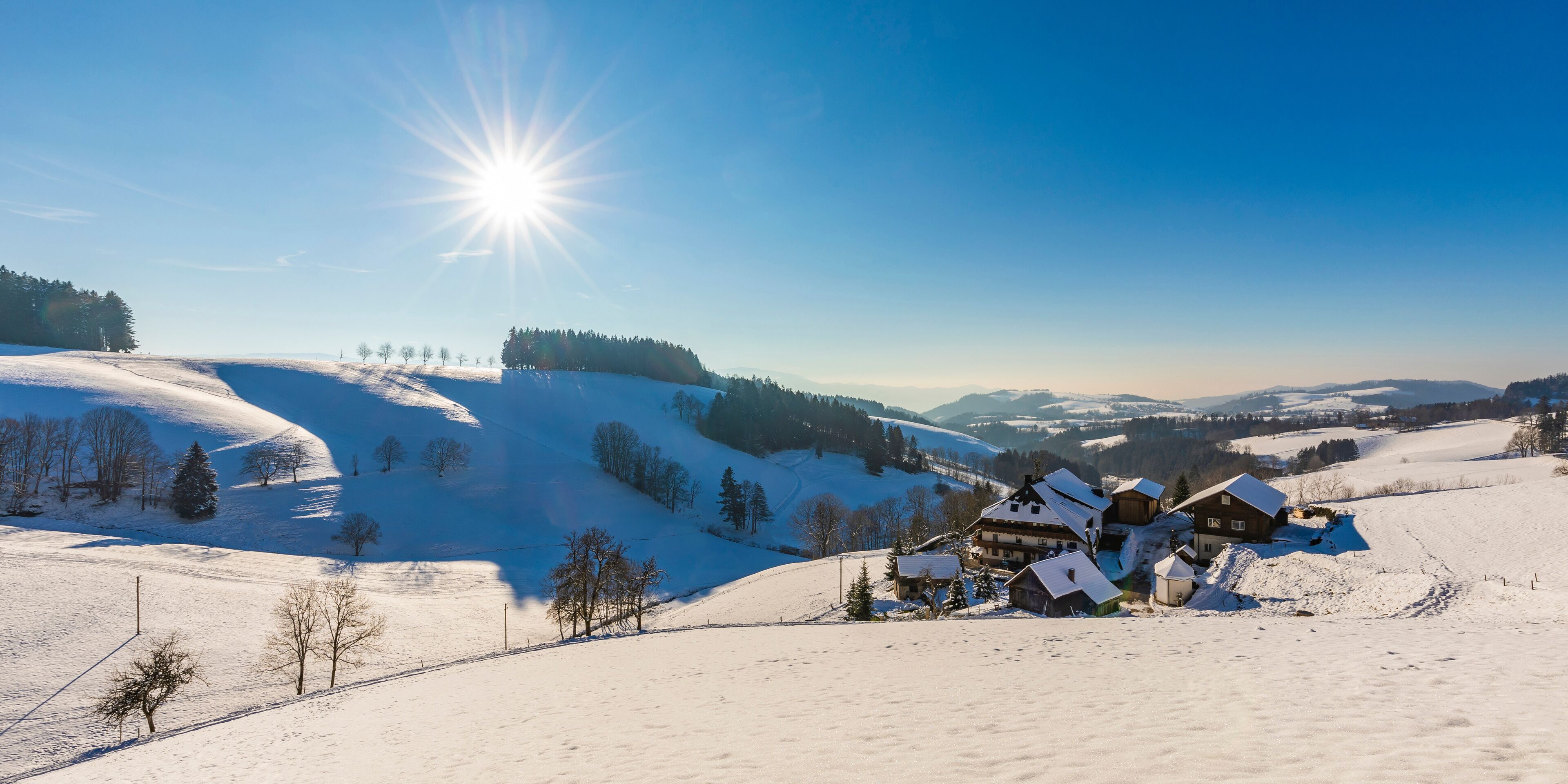 Germany, Baden-Wurttemberg, Sankt Margen, Sun shining over houses of town in middle of Black Forest in winter