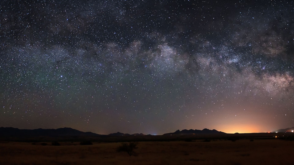 A starry night sky over a desert landscape with mountains in the distance.