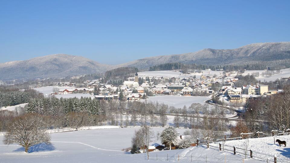 A snow-covered village with houses, a church, and mountains in the background.