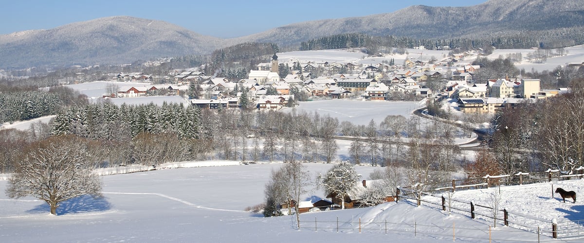 A snow-covered village with houses, a church, and mountains in the background.