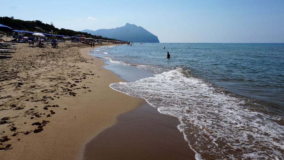 A sandy beach with umbrellas, a clear sky, and a mountain in the distance.