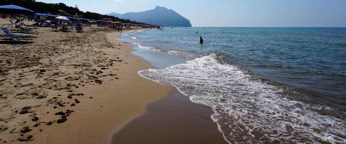 A sandy beach with umbrellas, a clear sky, and a mountain in the distance.