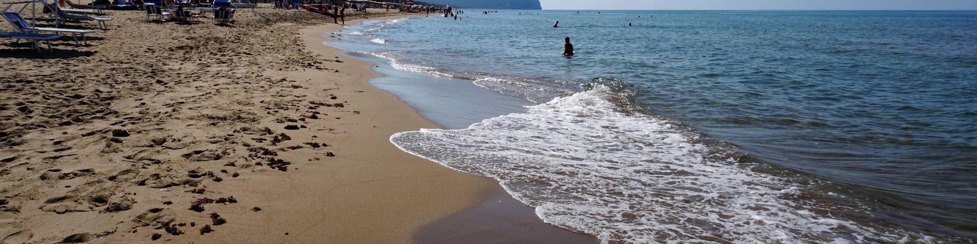 A sandy beach with umbrellas, a clear sky, and a mountain in the distance.