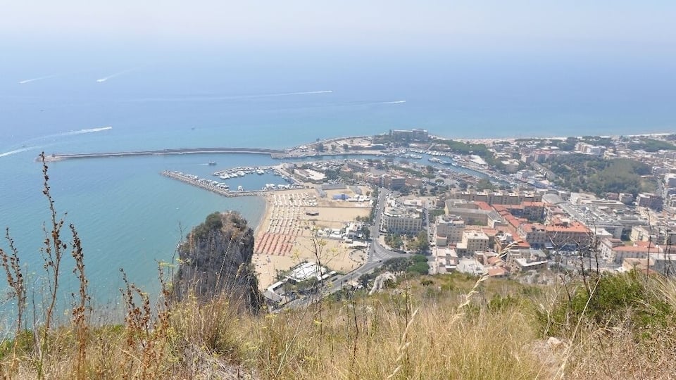 A coastal city with a beach, a pier, and a hilly landscape.