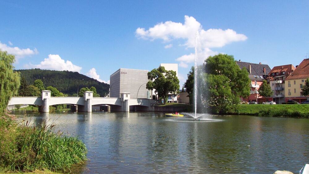A bridge over a river, a fountain, and buildings in the background.