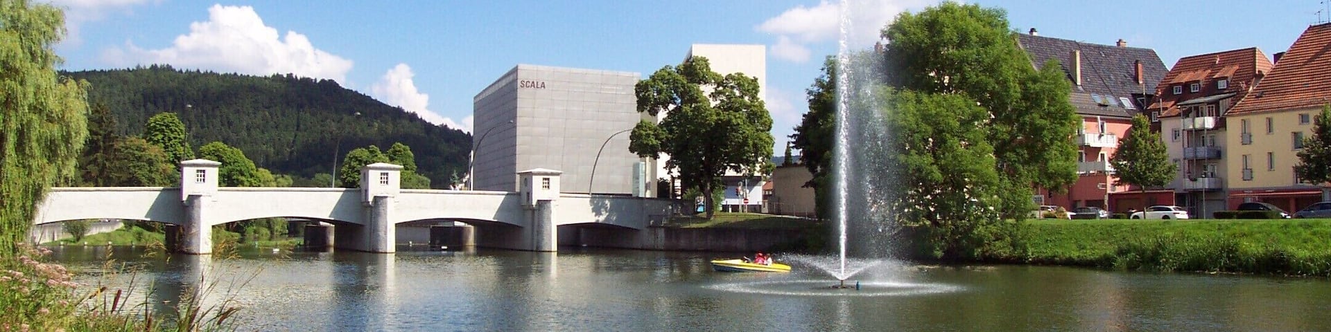 A bridge over a river, a fountain, and buildings in the background.