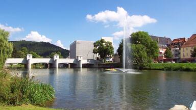 Uma ponte sobre um rio, uma fonte e edifícios ao fundo.