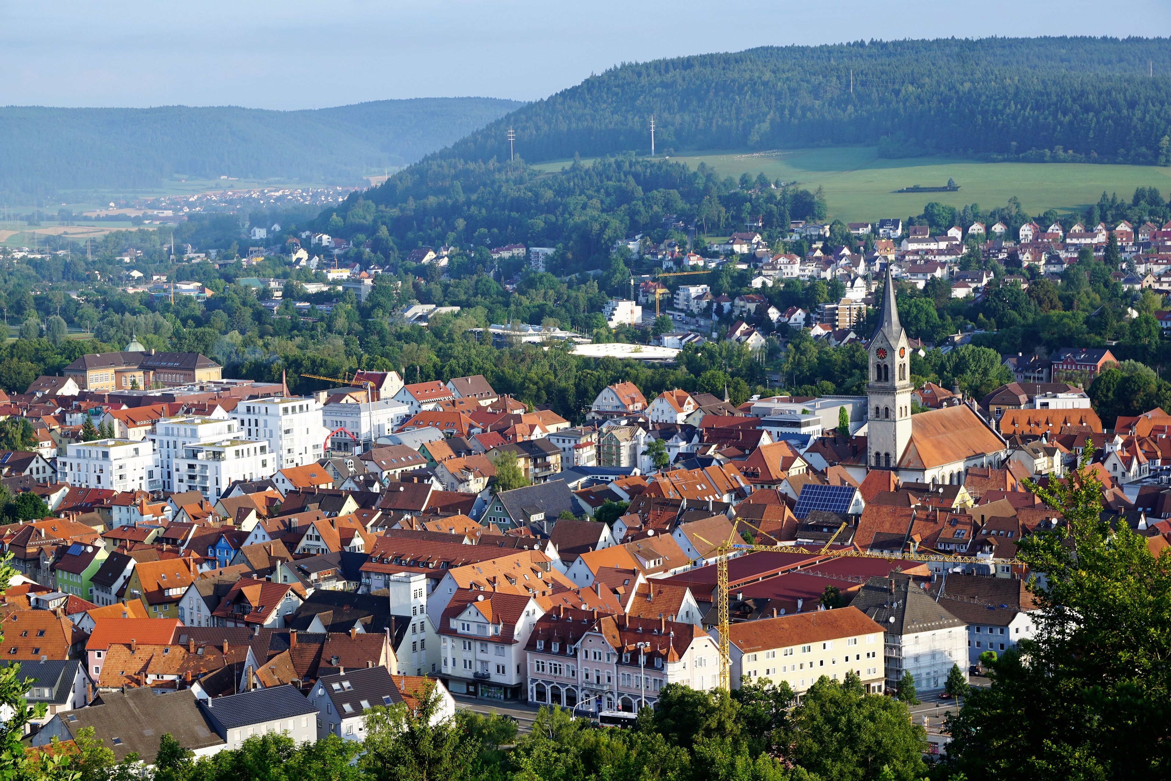 A town with red-roofed buildings, a church with a tall steeple, and a hill in the background.
