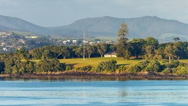 A coastal landscape with a body of water, a golf course, and a mountain range in the background.