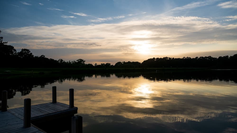 the sun sets over a pier and a lake one summer evening
