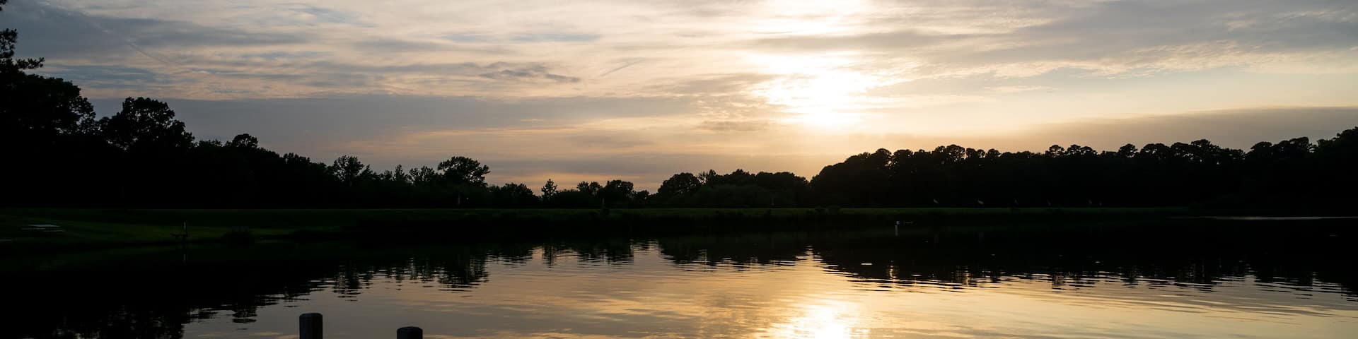 the sun sets over a pier and a lake one summer evening