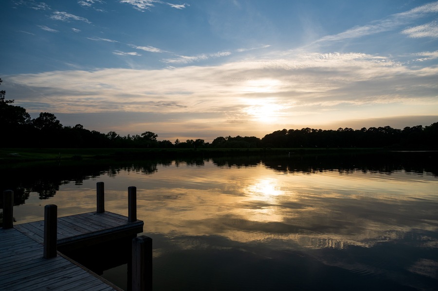 the sun sets over a pier and a lake one summer evening