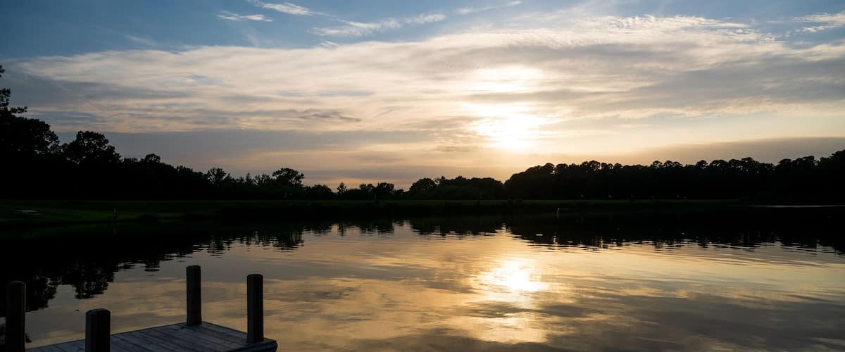 A calm lake at sunset with a wooden dock and trees in the background.
