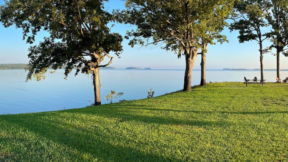 A lakeside view with a grassy area, trees, and a dock extending into the water.