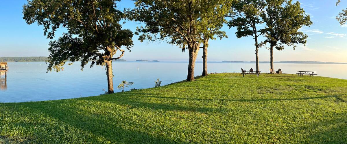 A lakeside view with a grassy area, trees, and a dock extending into the water.