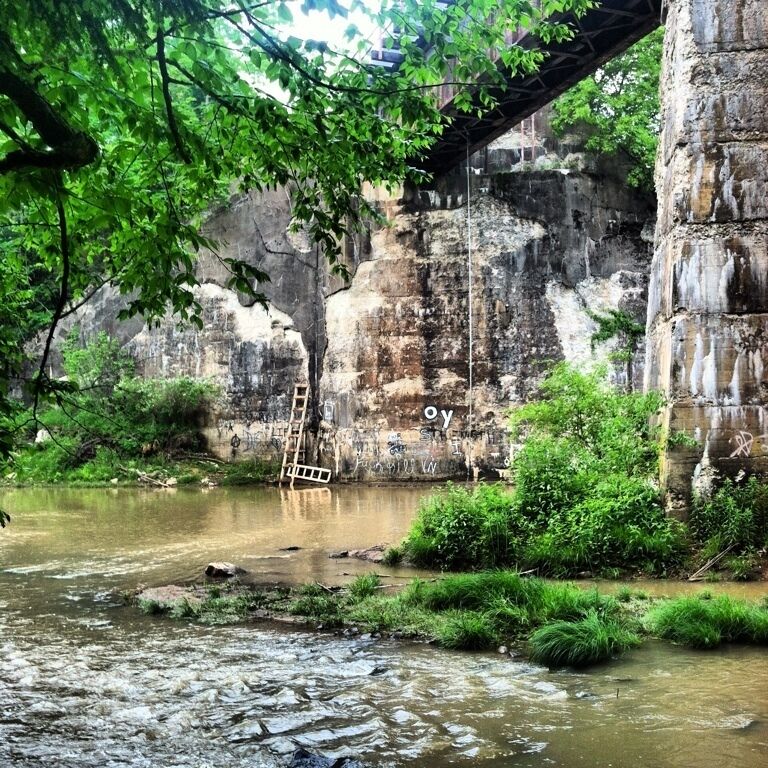 A river flowing under a bridge with a ladder leaning against the rock wall.