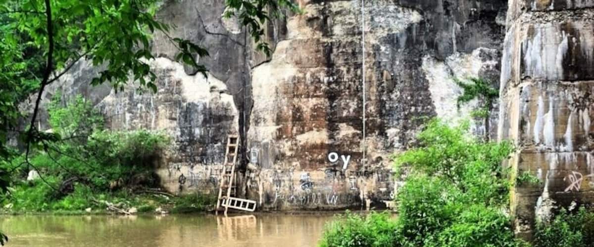 A river flowing under a bridge with a ladder leaning against the rock wall.