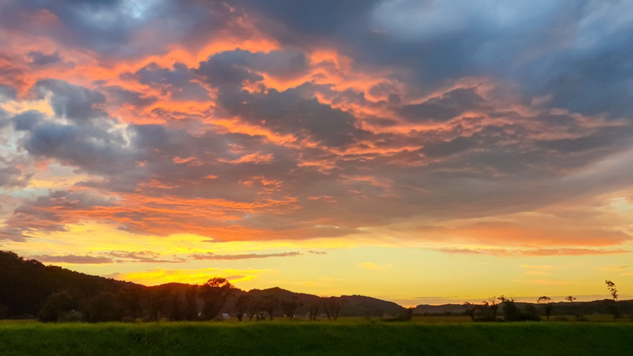 Dramatic sky in Jennersdorf, Burgenland, Austria. Thick swirling clouds painted in hues of gray, orange, pink. Sunset of warm glow creating breathtaking spectacle. Silhouette of rolling hill landscape