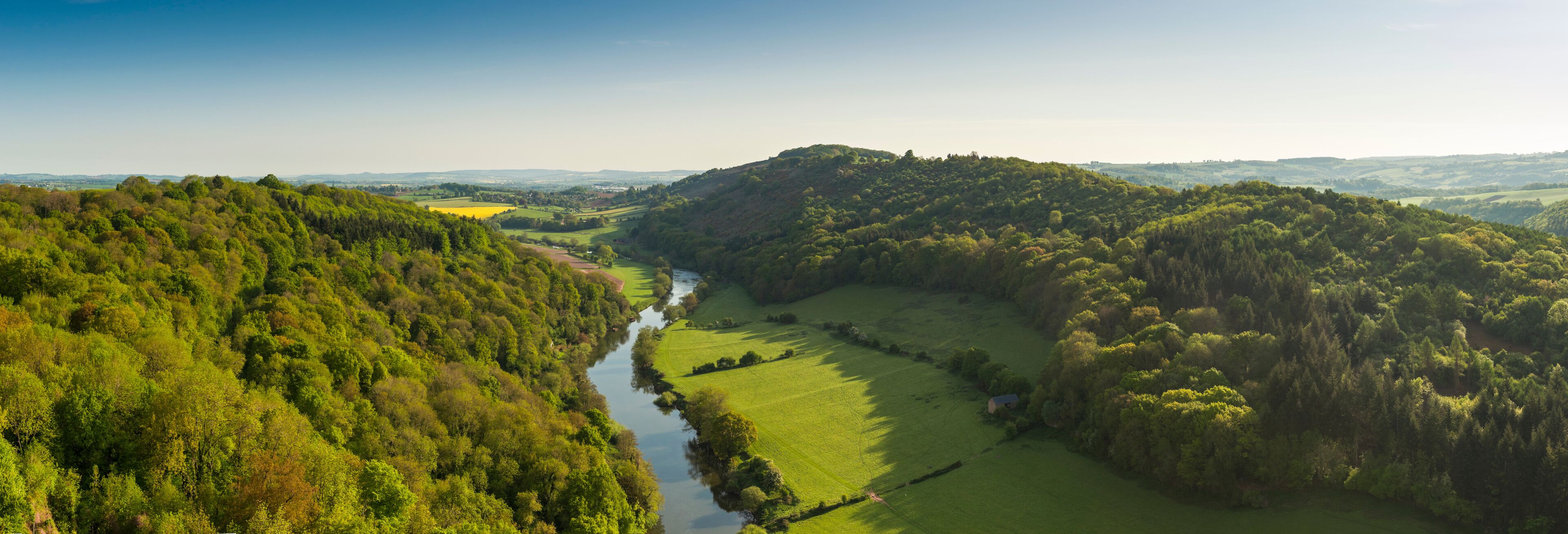 A river winding through a lush valley surrounded by dense forests and rolling hills.