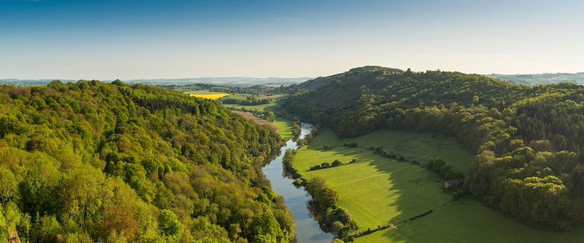 A river winding through a lush valley surrounded by dense forests and rolling hills.