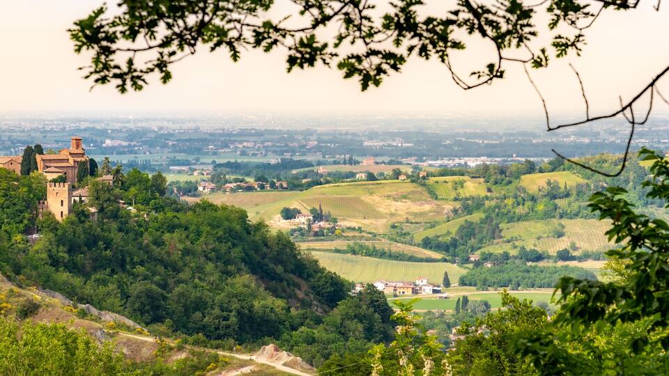 A castle on a hill overlooking a valley with fields and distant buildings.
