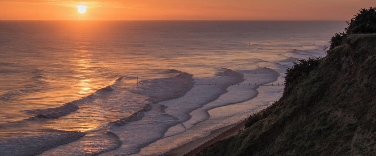 A sunset over a coastal landscape with waves gently crashing onto the shore.