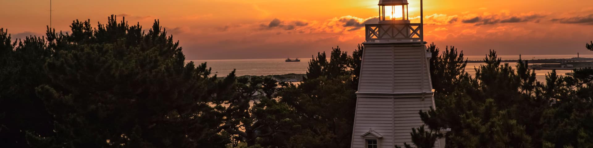 A lighthouse at sunset with a clear sky and silhouettes of trees.