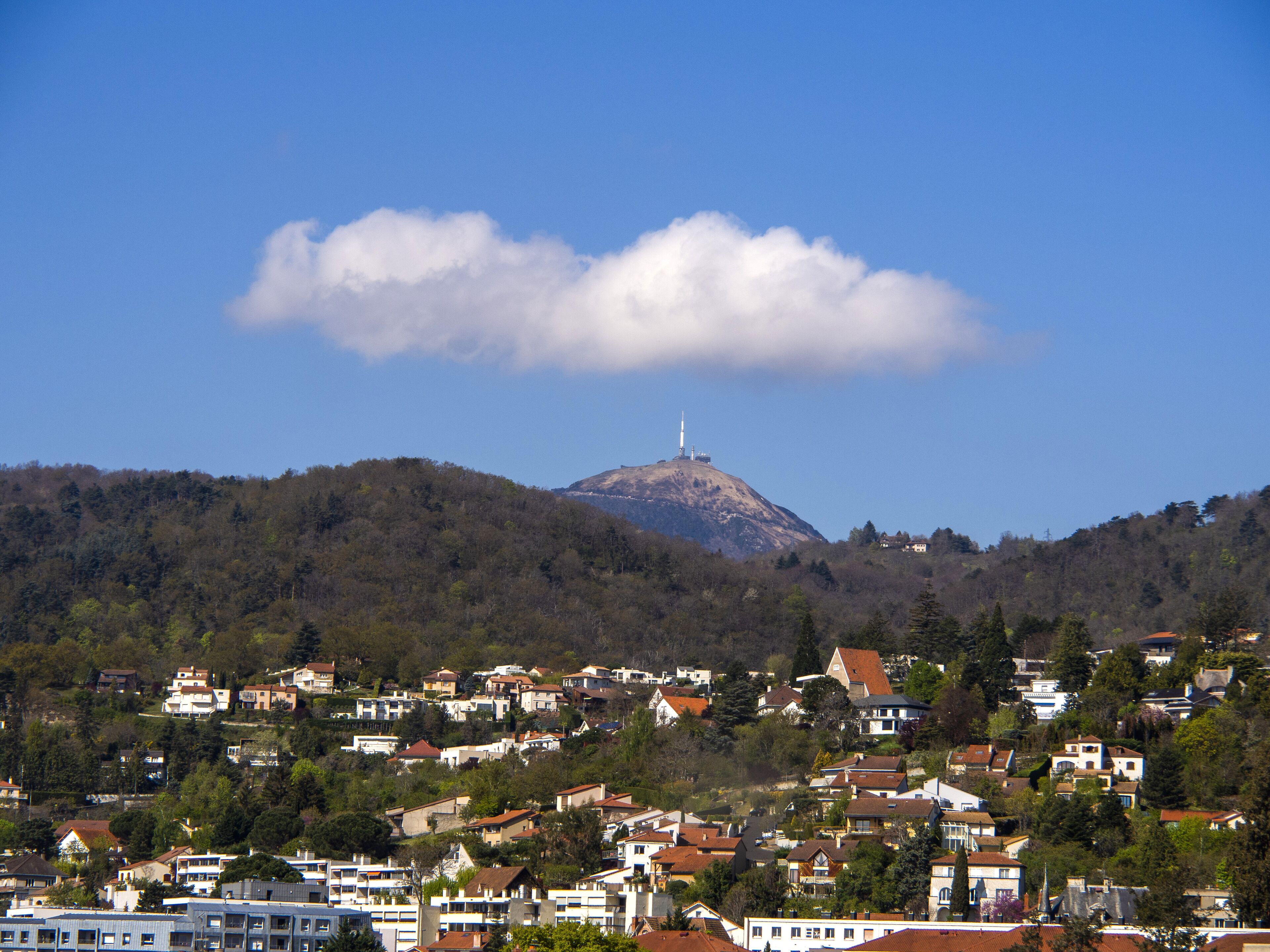 A town with houses on a hillside, a prominent hill with a tower, and a partly cloudy sky.