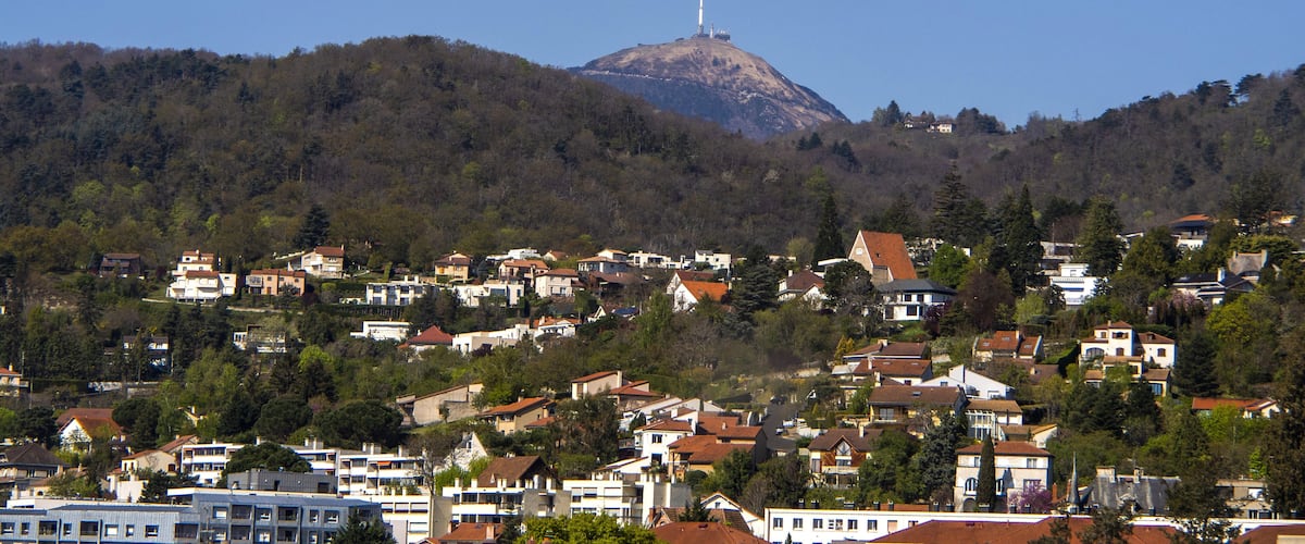 A town with houses on a hillside, a prominent hill with a tower, and a partly cloudy sky.