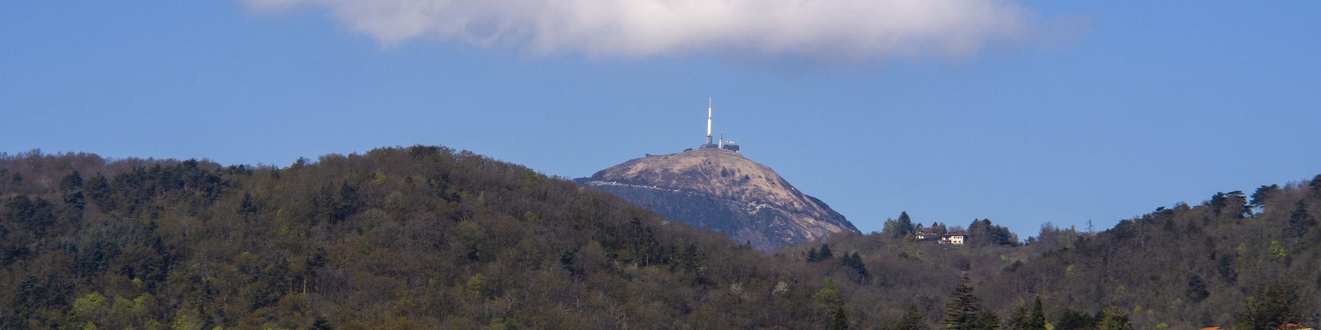 A town with houses on a hillside, a prominent hill with a tower, and a partly cloudy sky.