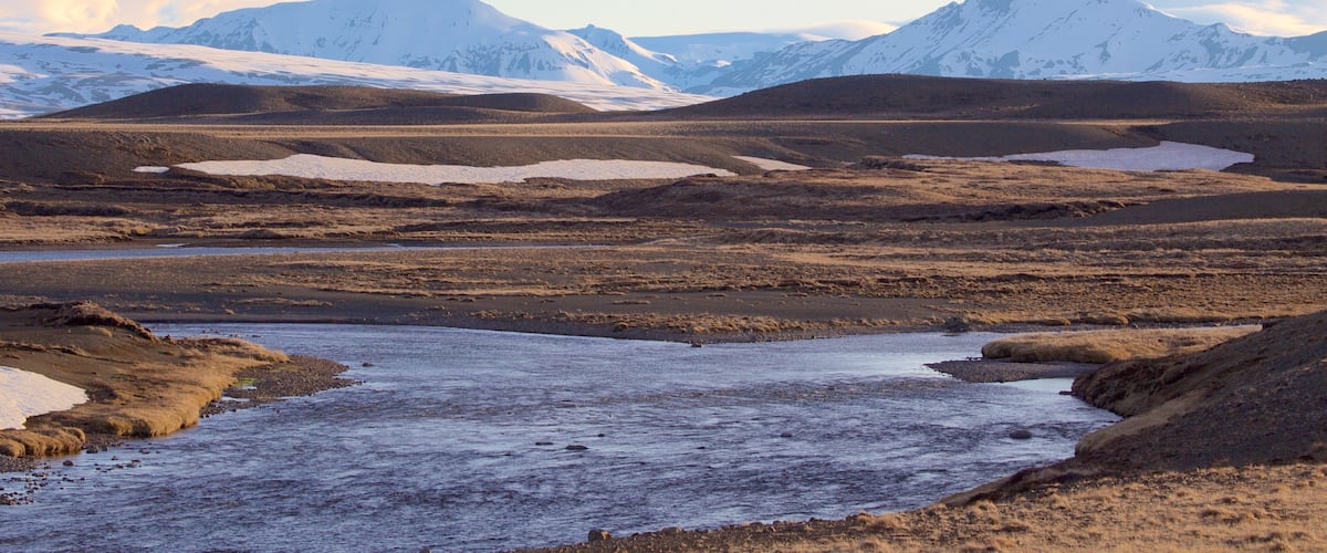 A snow-covered landscape with mountains in the background and a river in the foreground.