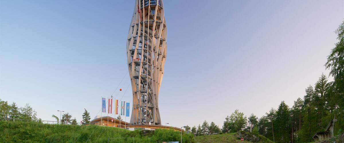 A tall, spiraling tower with a unique architectural design, surrounded by greenery and flags.